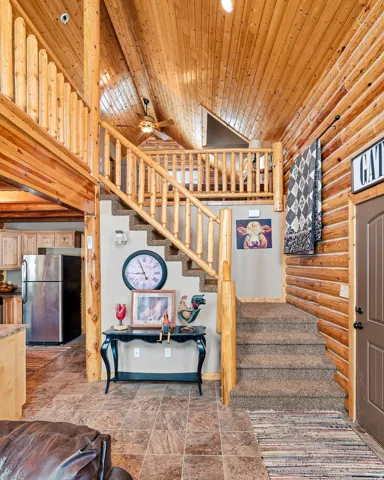 Vaulted natural wood plank ceiling, natural wood log walls, natural wood log railings, carpeted stairs, and tiled flooring