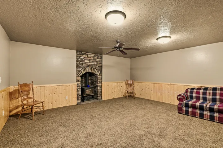 Stone fireplace with arched opening, wood-paneled wainscoting, textured ceiling, ceiling fan, and flush-mount lighting fixtures