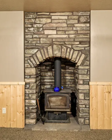Stacked stone fireplace with an arched opening, wood-burning stove, and natural wood wainscoting