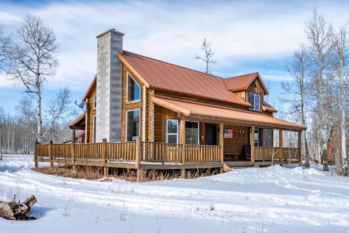 Log cabin exterior featuring a covered porch, a wraparound deck, a metal roof, and a prominent stone-clad chimney