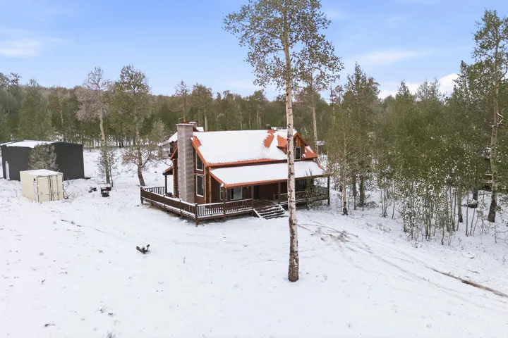 Wood-sided cabin-style residence featuring a stone chimney, covered front porch, and a surrounding deck