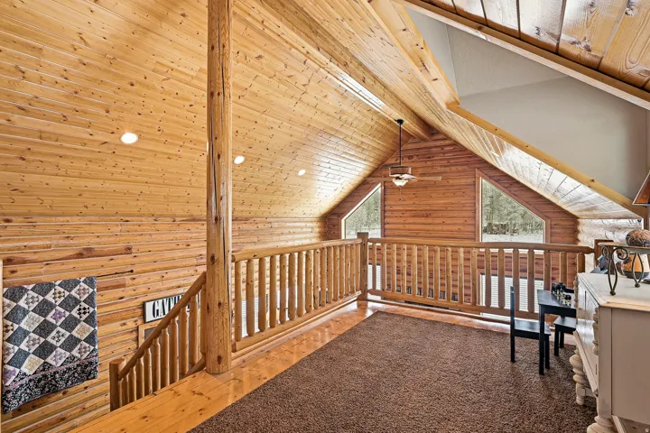 Vaulted wood-paneled ceiling with exposed wood beams, log railing, two triangular windows, and recessed lighting