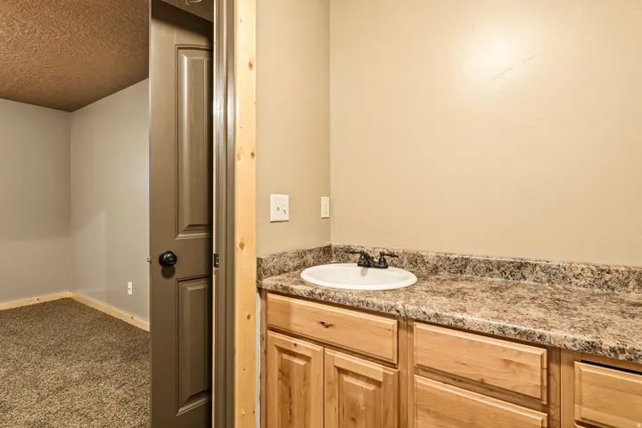 Built-in vanity with a circular sink, dark counter, and light wood cabinetry