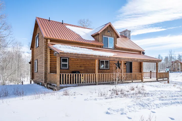 Log cabin exterior featuring a covered porch, wood railing, metal roof, and stone chimney