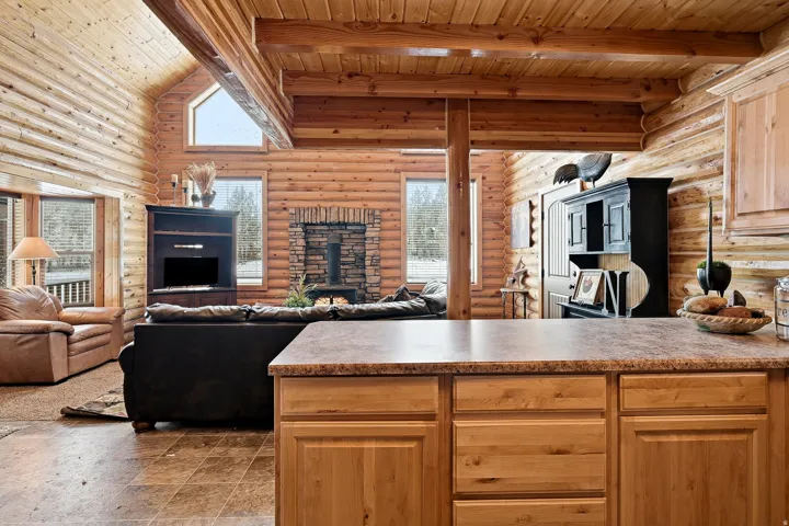 Exposed wood beam ceiling with a vaulted design, wood-paneled walls, built-in fireplace with a stone surround, wood-finish cabinetry, and a stone-look countertop