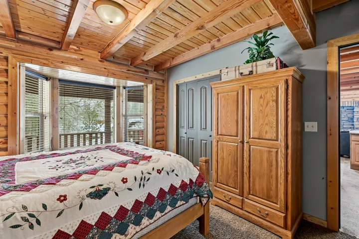 Exposed wood ceiling beams, wood paneling, bay window with blinds, and built-in closet with bifold doors