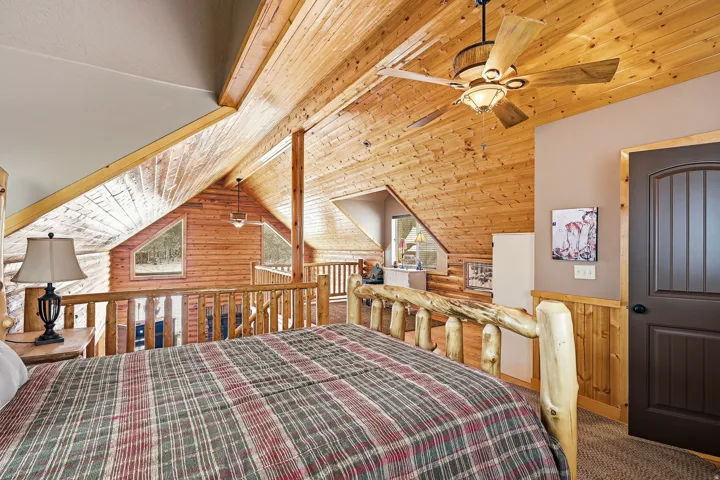 Spacious loft bedroom showcasing exposed wood beam cathedral ceilings, wood-finish flooring, and a ceiling fan with integrated lighting