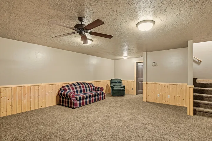 Carpeted floor, wood paneling, ceiling fan, flush-mount lighting, and an internal staircase