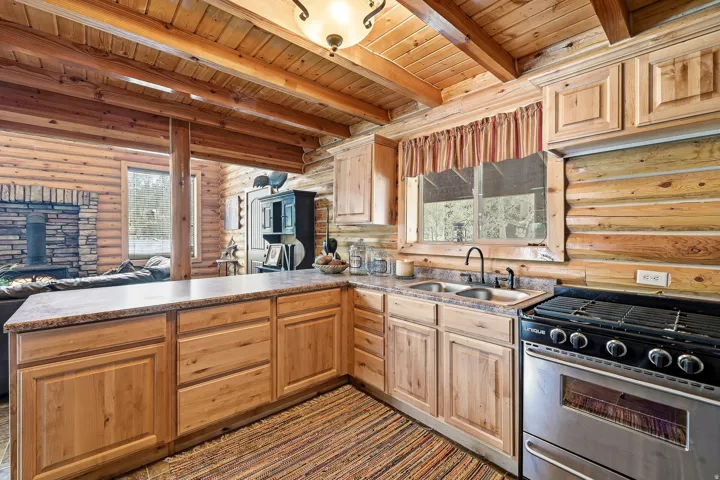 Wood-finish cabinetry, stainless steel range, double basin sink, and exposed wood beam ceiling