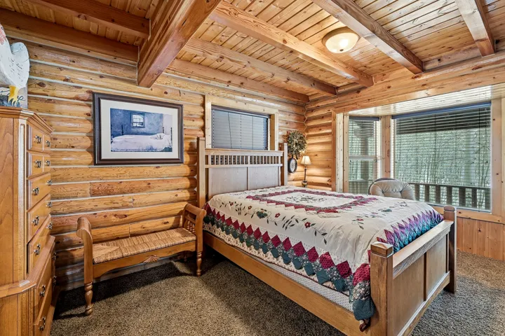 Log wall construction, wood-paneled ceilings, and multiple windows with horizontal blinds
