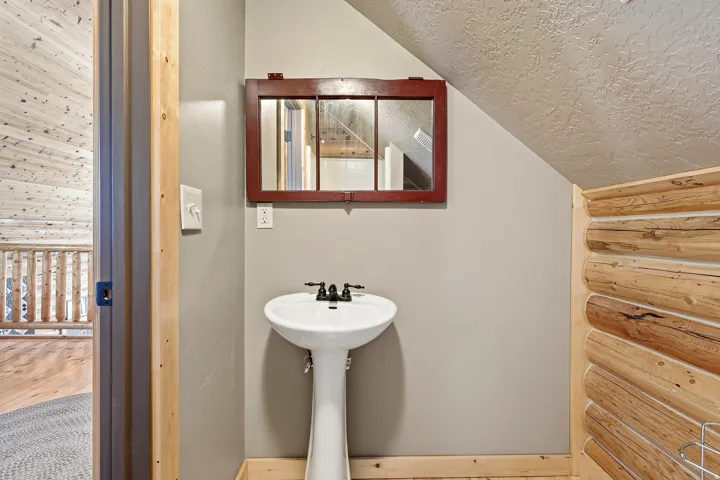 Pedestal sink with a dark bronze faucet, framed mirror, and log-style wall paneling