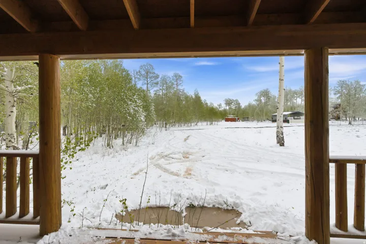 Wood-beam porch with wooden railing overlooking a snow-covered landscape featuring mature trees