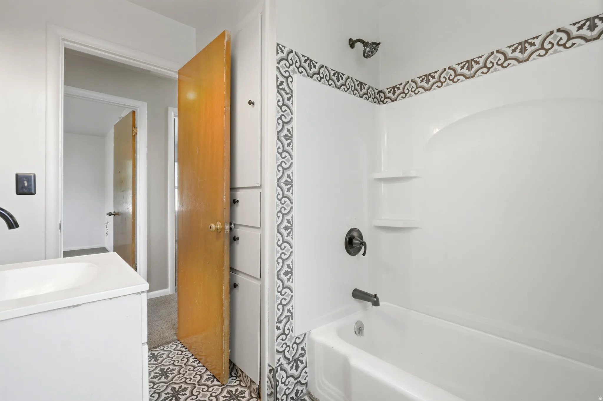 White vanity with integrated sink, patterned floor tile, built-in storage cabinetry, and a white tub with dark bronze fixtures