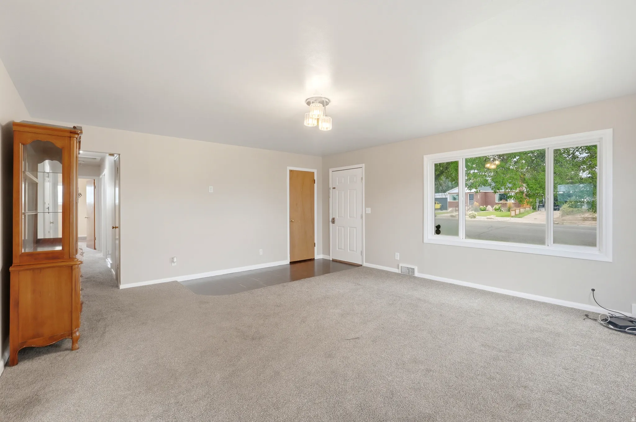 Expansive carpeted area with neutral wall tones and a wide window offering abundant natural light