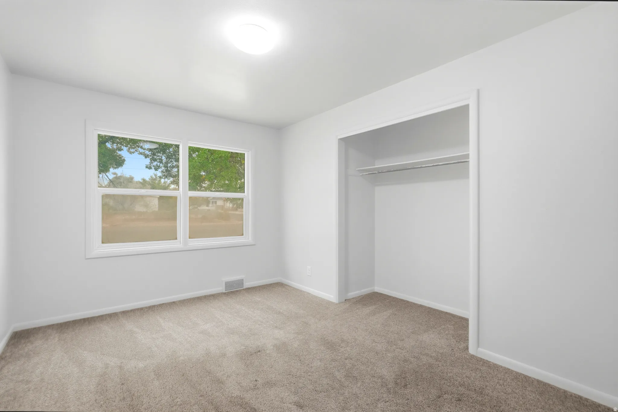 Neutral wall paint, carpeting, double-pane window, and an integrated closet with shelving and a hanging rod