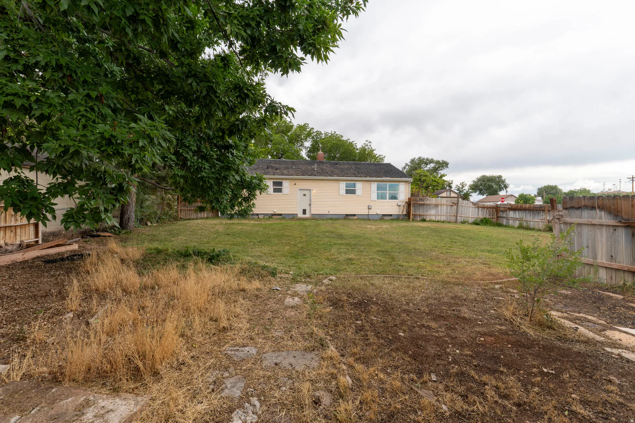 Expansive rear yard featuring a manicured lawn, established perimeter fencing, and a mature shade tree
