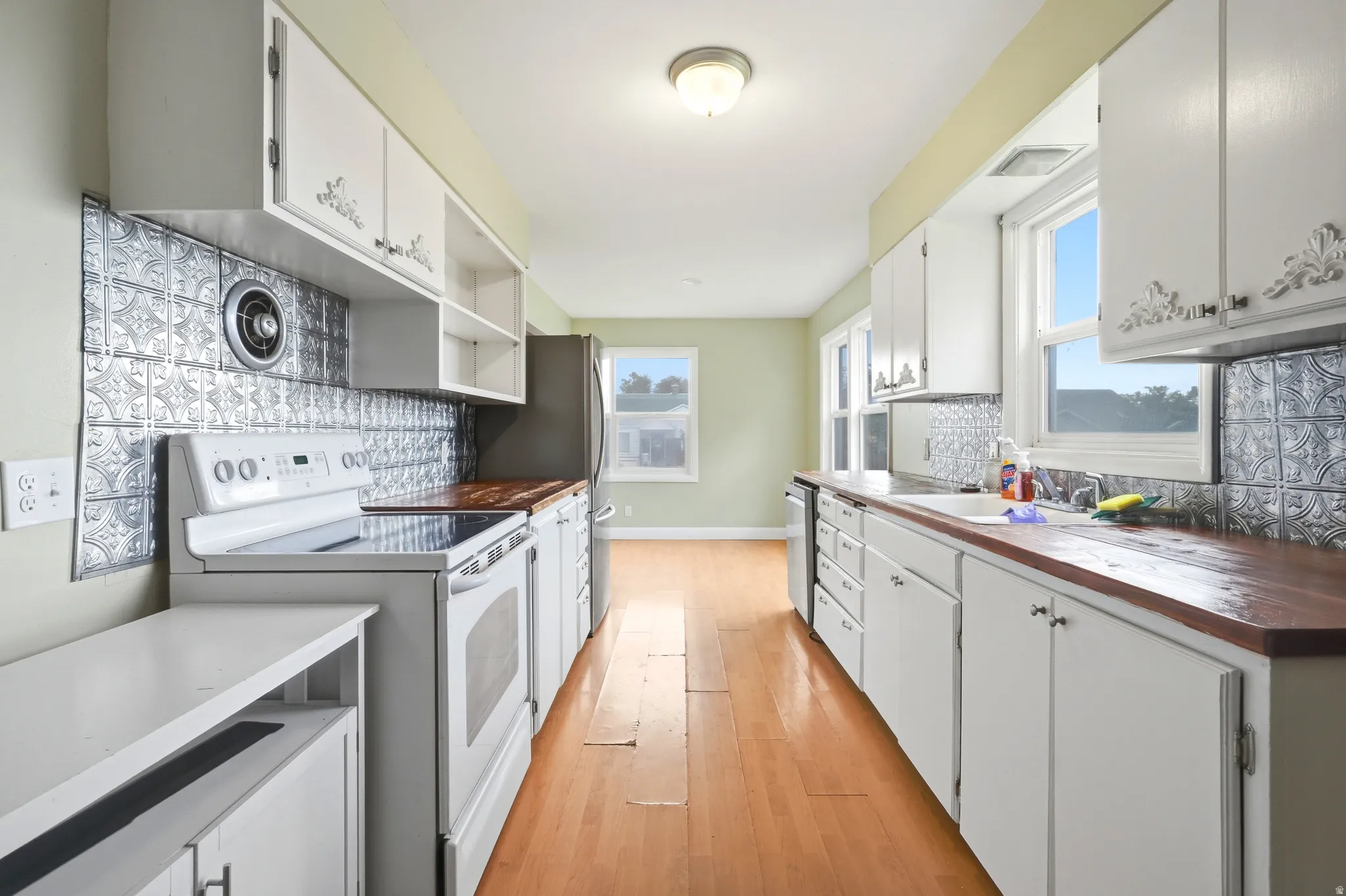 Galley kitchen featuring white cabinetry, wood-finish countertops, stainless steel appliances, a tin-panel backsplash, and hardwood flooring