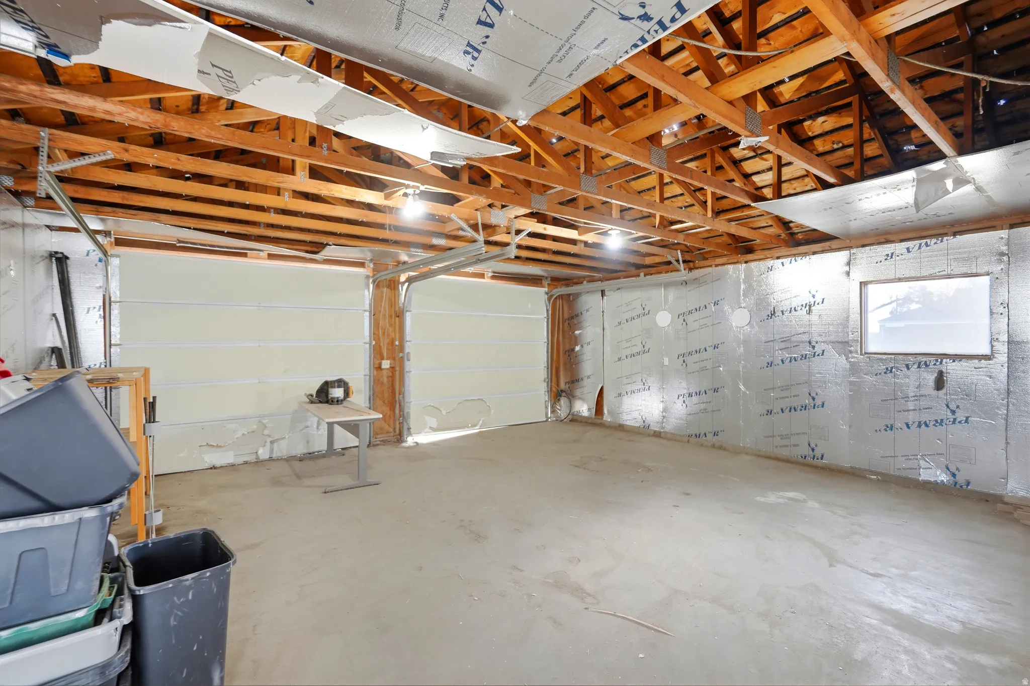 Exposed wood ceiling beams with recessed lighting, concrete flooring, and two overhead garage doors