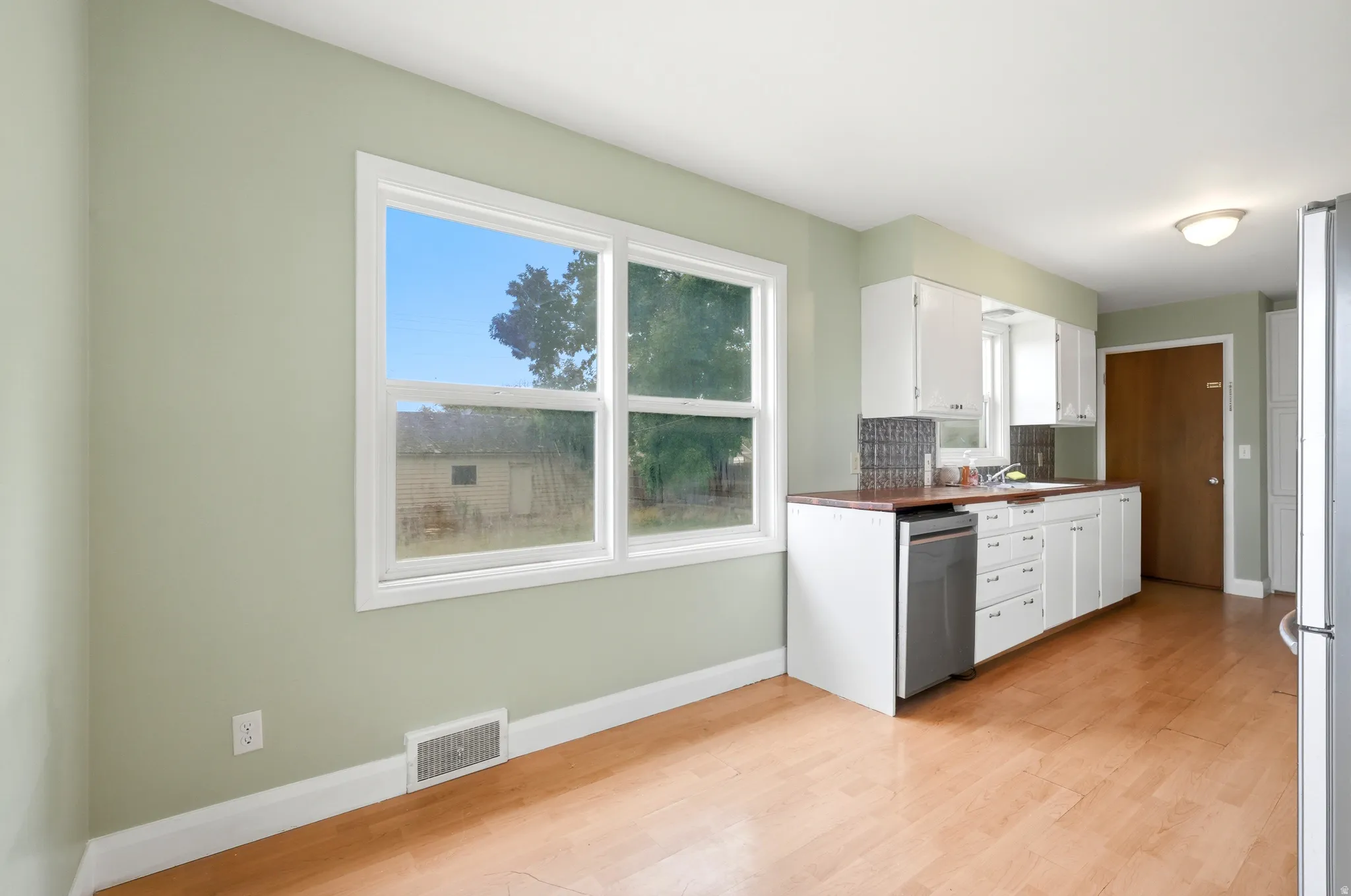 Kitchen area featuring wood-finish flooring, white cabinetry, a stainless steel dishwasher, and a window with white trim
