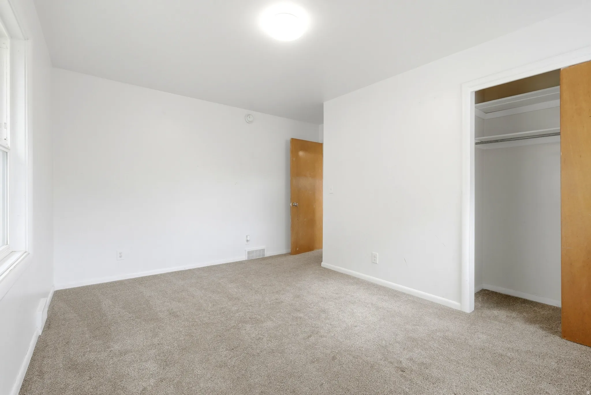 Neutral tone carpeted flooring, white painted walls, natural wood-finish door, and a built-in closet with sliding doors