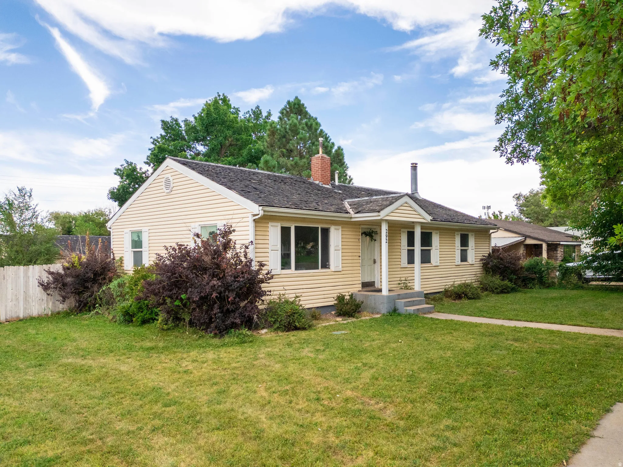 Ranch-style exterior with horizontal siding, a covered porch entry, a brick chimney, and a picket fence