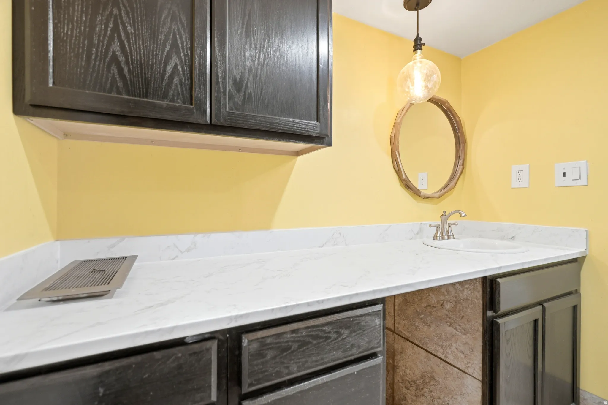 Dark wood-finish cabinetry, white countertop, integrated sink, and an overhead pendant light fixture