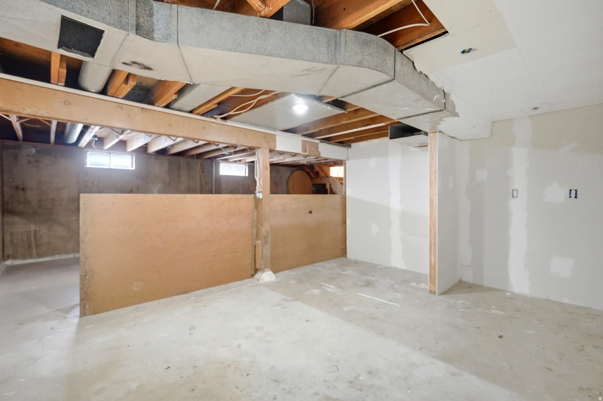 Unfinished basement with concrete flooring, exposed wood ceiling joists, and partially finished drywall