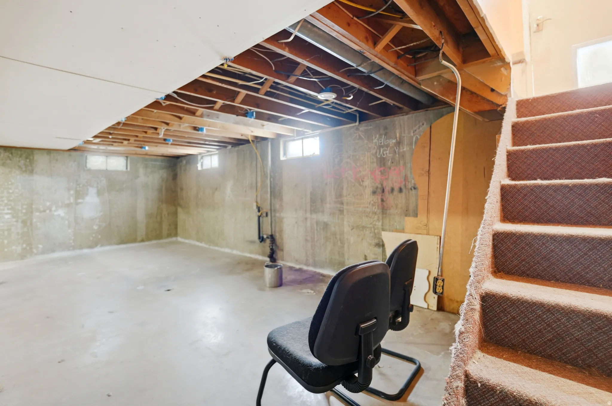 Unfinished basement space featuring exposed ceiling joists, concrete flooring, and multiple window openings