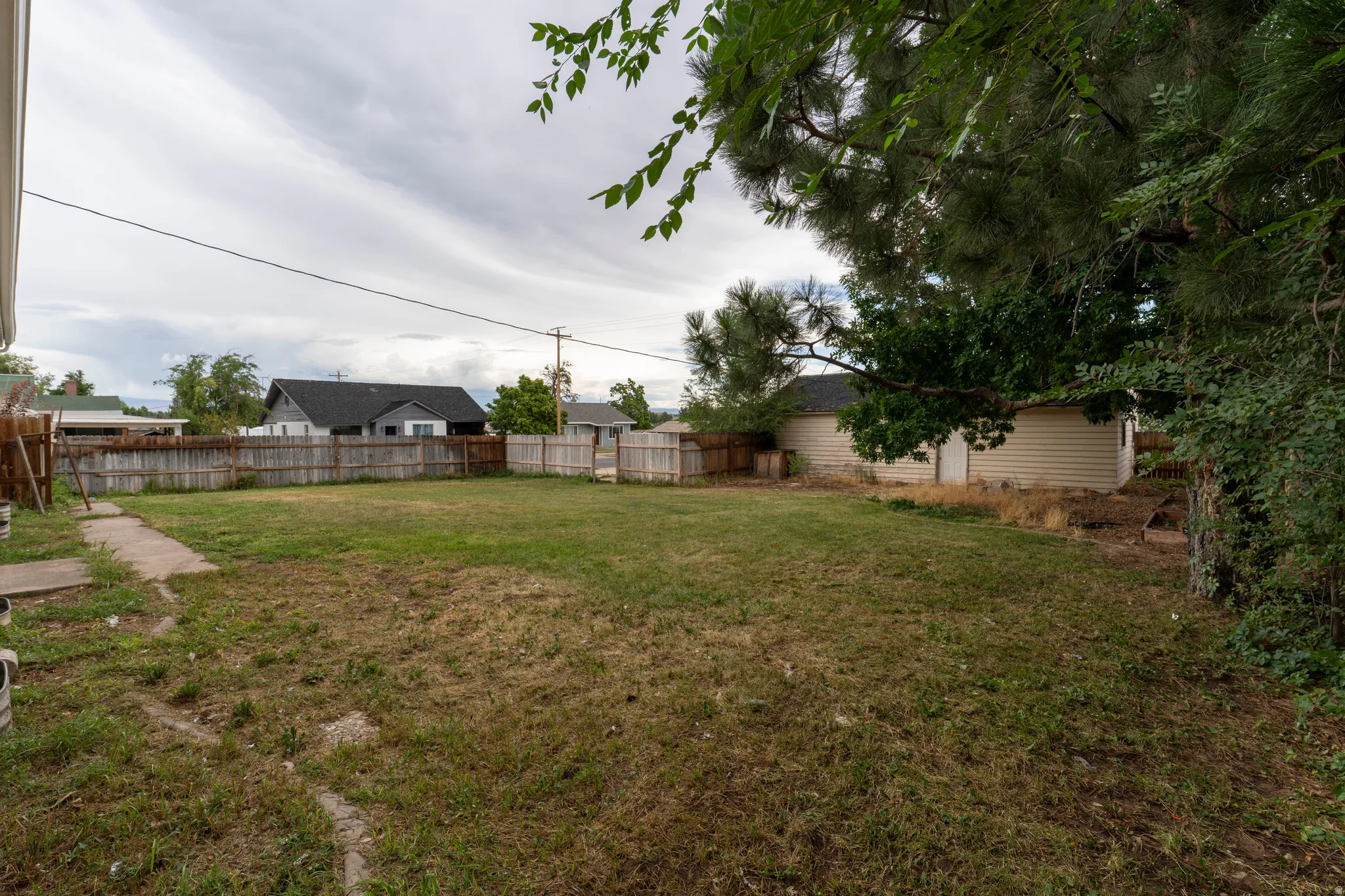 Expansive backyard with a wood privacy fence, concrete path, and mature trees