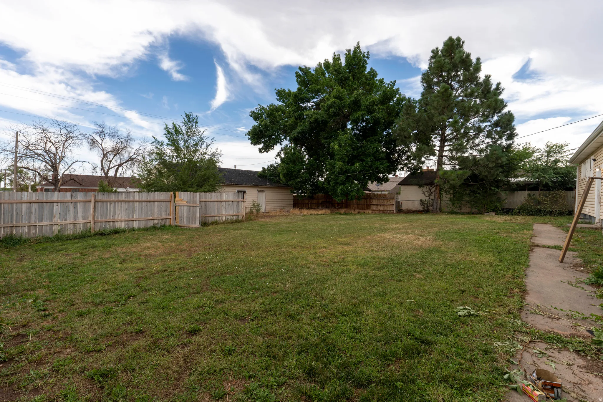 Expansive backyard featuring a wood privacy fence, mature trees, a concrete pathway, and a detached structure
