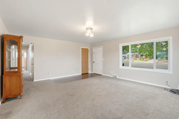 Expansive carpeted area with neutral wall tones and a wide window offering abundant natural light