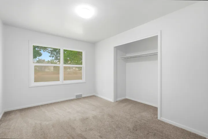 Neutral wall paint, carpeting, double-pane window, and an integrated closet with shelving and a hanging rod