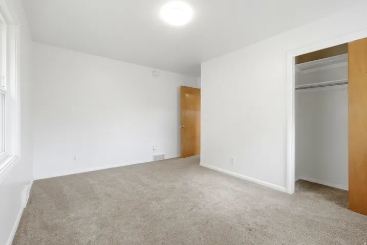 Neutral tone carpeted flooring, white painted walls, natural wood-finish door, and a built-in closet with sliding doors