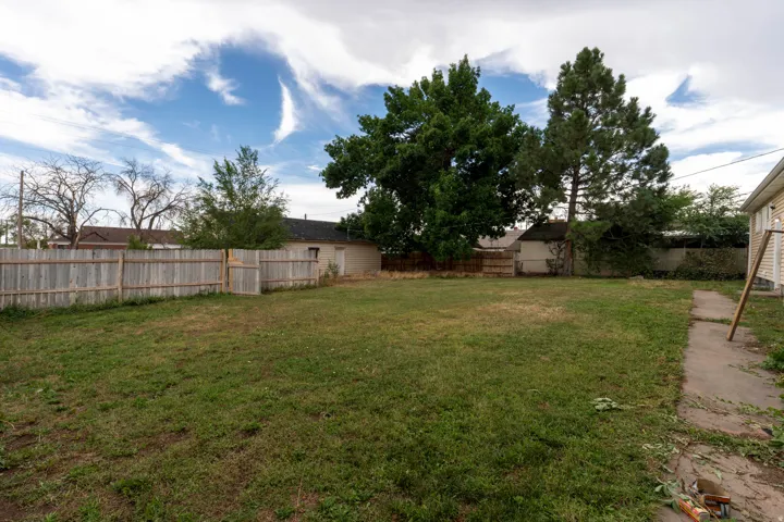 Expansive backyard featuring a wood privacy fence, mature trees, a concrete pathway, and a detached structure