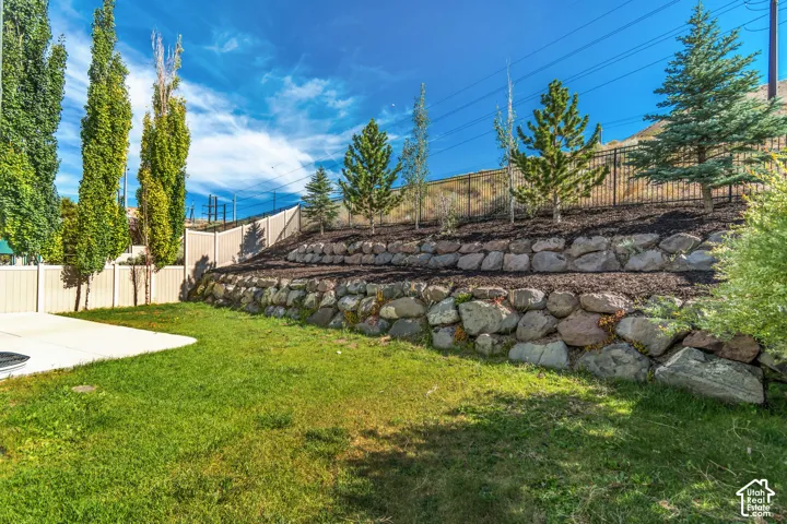 Expansive backyard featuring a stone retaining wall, manicured lawn, paved patio, and mature trees