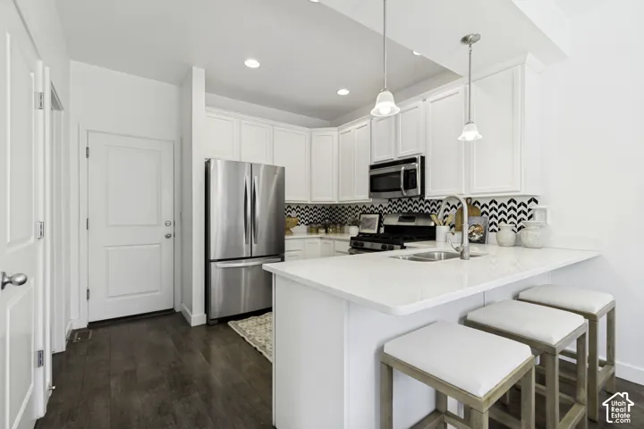 Kitchen featuring white cabinetry, stainless steel appliances, a chevron pattern backsplash, and a breakfast bar with pendant lighting