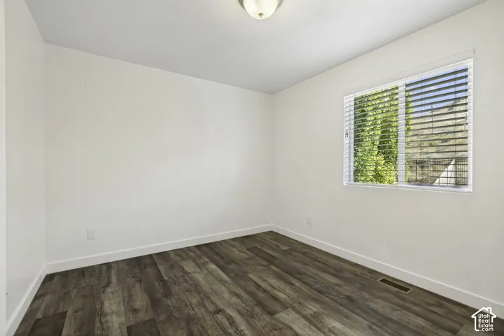 White walls with wood-finish flooring, a single window with blinds, and a ceiling-mounted light fixture