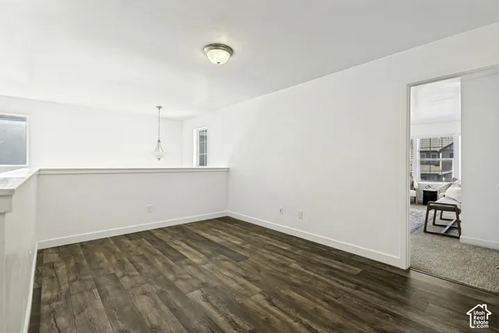 Spacious room featuring rich wood-finish flooring, white shiplap wainscoting, ceiling-mounted light fixture, and generous natural light from multiple windows