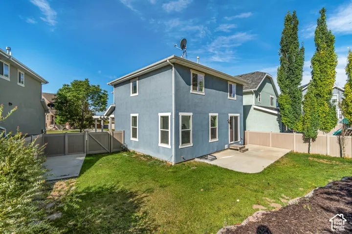 Stucco exterior with multiple windows, sliding glass door, concrete patio, and fenced yard