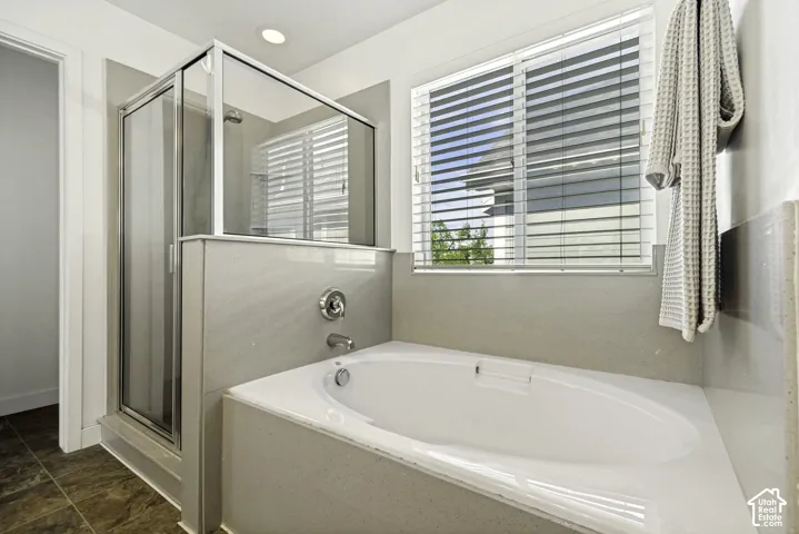 Built-in soaking tub with chrome fixtures, an adjacent glass-enclosed shower, and a large window with horizontal blinds