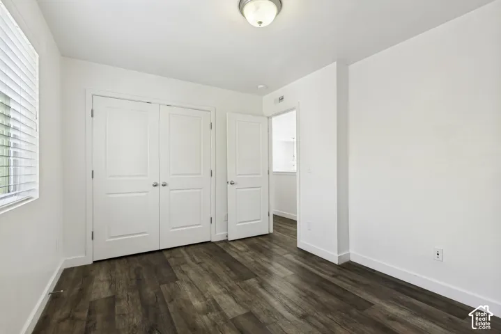 Wood-finish flooring, white walls, white trim, white window blinds, and a built-in closet with white bifold doors