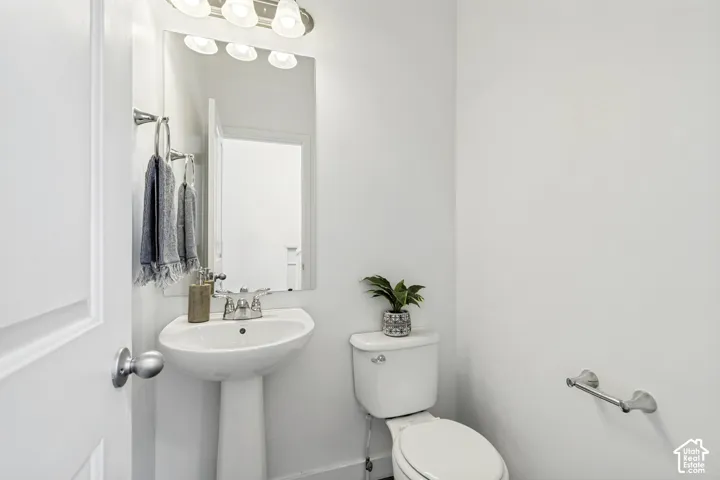 Pedestal sink with chrome faucet, wall-mounted mirror, and vanity light fixture