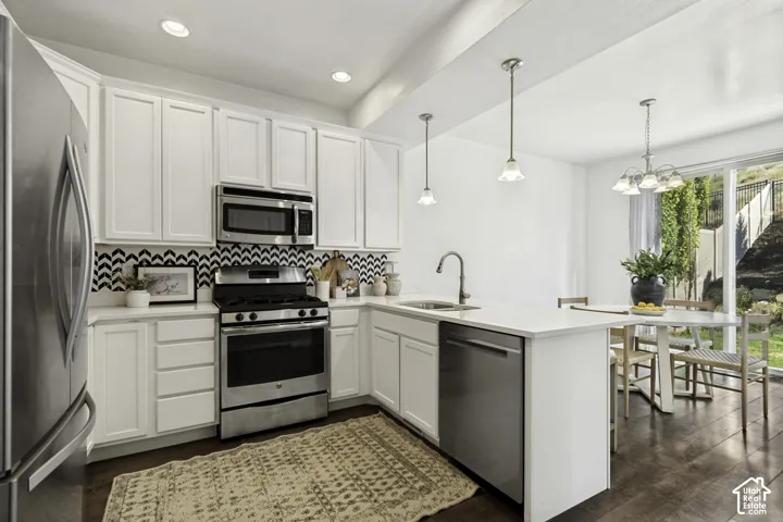White cabinetry, stainless steel appliances, chevron pattern backsplash, wood-finish flooring, and a sliding glass door to the exterior