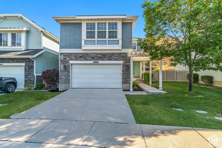 Two-story residence featuring a stone and stucco facade, an integrated garage, a covered front entryway with a pergola, and a concrete driveway