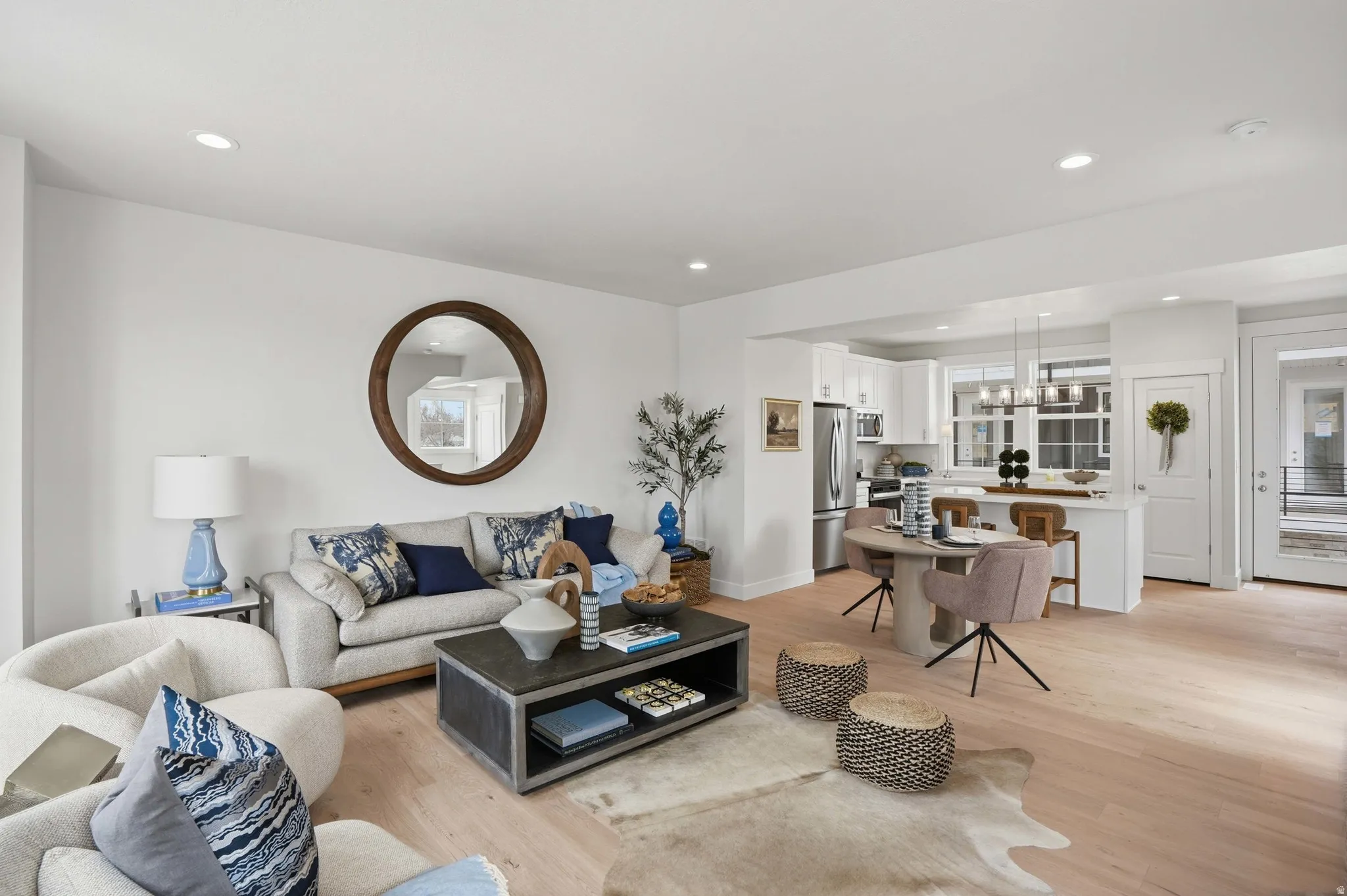 Recessed ceiling lighting, light wood-finish flooring, white walls, kitchen with white cabinetry, and stainless steel appliances