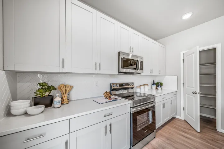 White shaker-style cabinetry, stainless steel appliances, light-toned countertops, white herringbone tile backsplash, and wood-finish flooring