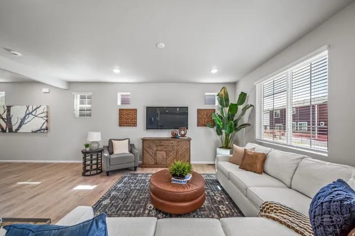 Recessed lighting illuminates the open living space, featuring wood-finish flooring and multiple windows with blinds