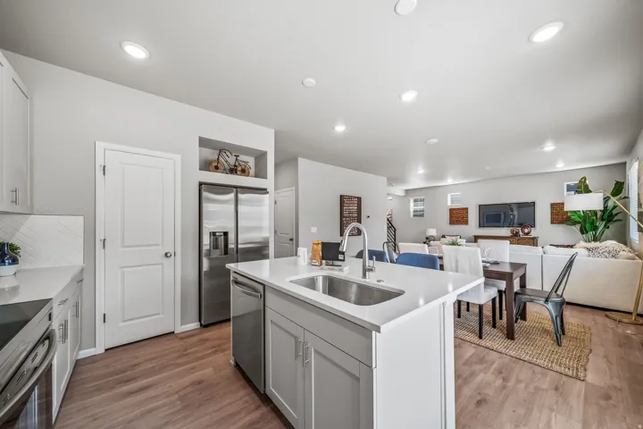 Kitchen featuring light-toned cabinetry, stainless steel appliances, a center island with an undermount sink, and wood-finish flooring
