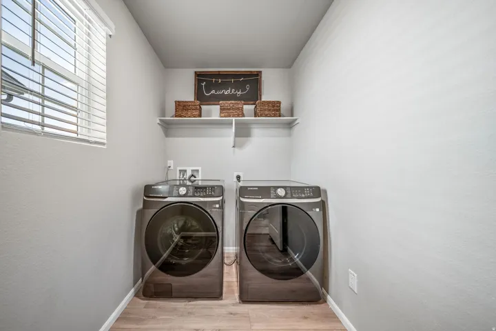 Laundry area featuring wood-finish flooring, a window with blinds, and an overhead shelf
