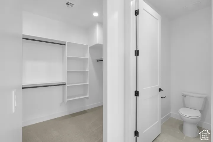 White built-in shelving, hanging rods, recessed lighting, white door with black hardware, and a toilet with tile flooring